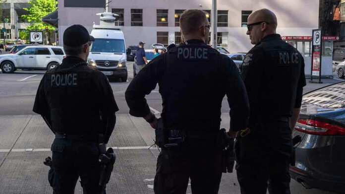 1386794081 Three police officers standing on a city street.