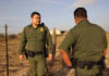 Two uniformed officers standing outdoors near a fence.