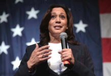 Woman speaking with microphone, American flag background.