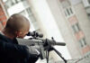 Snipers on Rooftops Fuels Alarm Person aiming a rifle from a building balcony.
