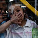 A child covering their face while looking through a glass window