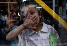 A child covering their face while looking through a glass window