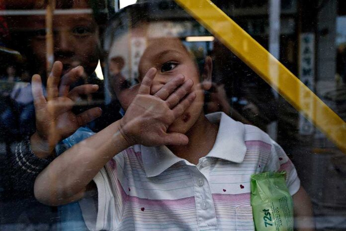 shutterstock_1090186736.jpg A child covering their face while looking through a glass window