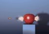 A red apple being struck by a bullet, showing an explosion effect