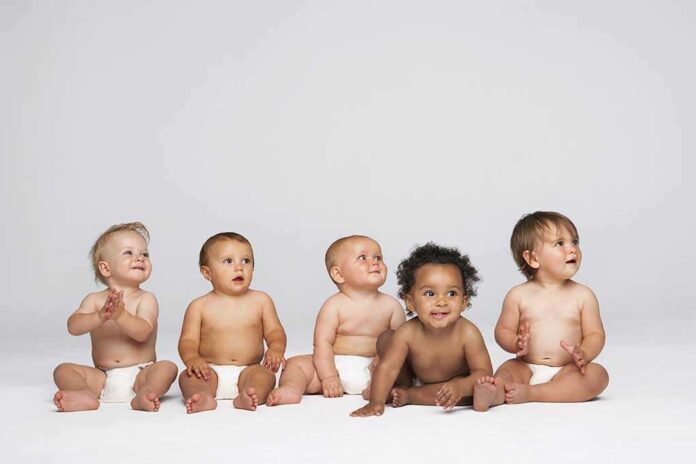 Five diverse babies sitting on a neutral background, displaying playful expressions