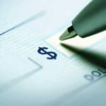 Billionaire SAVES Troops When Government FAILS Close-up of a pen poised over a check with a dollar sign