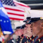 U.S. Marines in uniform standing in formation with flags in the background