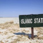 U.S. Religion Shocker — Islam US GROWTH A weathered sign reading ISLAMIC STATE in a barren landscape