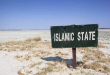 U.S. Religion Shocker — Islam US GROWTH A weathered sign reading ISLAMIC STATE in a barren landscape