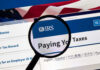 IRS Drops $5 Million Hammer—Senator Cornered Magnifying glass over IRS website for paying taxes.