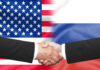 Hands shaking in front of USA and Russia flags.