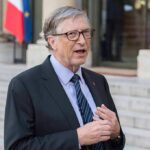 Shocking Revelation — Gates Exposes Climate Strategies’s Failures A man in formal attire speaking outdoors with a flag in the background