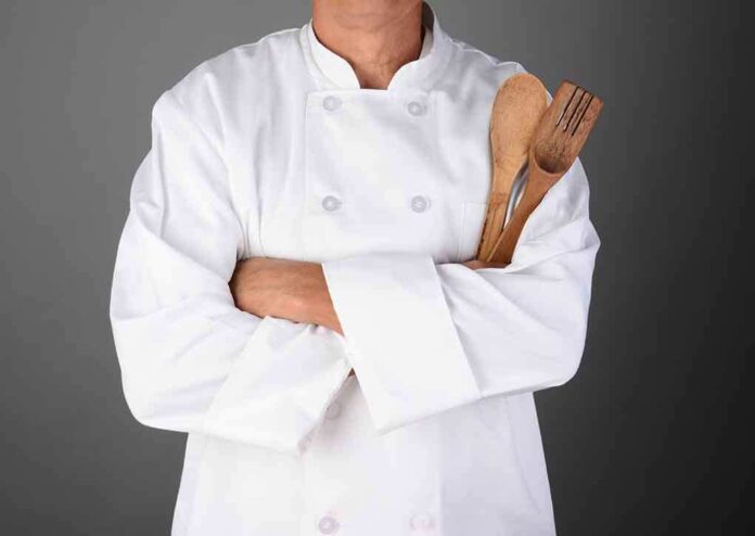 shutterstock_158666291.jpg A chef in a white uniform holding wooden cooking utensils with crossed arms