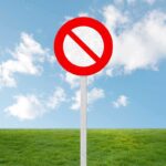 A no entry sign on a grassy field under a clear blue sky