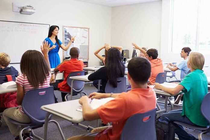 shutterstock_199144970.jpg Teacher in a blue dress instructing students in a classroom with hands raised