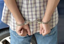 Employee Fights Intruder — Gets HANDCUFFED A person in handcuffs viewed from behind, wearing a plaid shirt and denim jeans