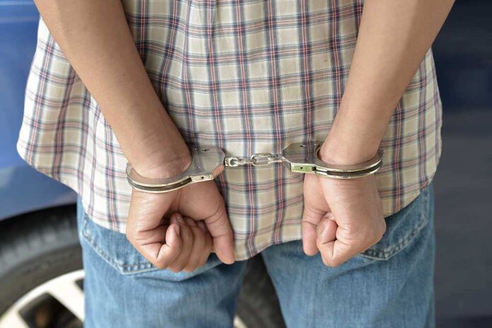shutterstock_215366989.jpg A person in handcuffs viewed from behind, wearing a plaid shirt and denim jeans