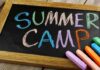Chalkboard with colorful writing that says Summer Camp and several pieces of chalk