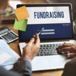 Two individuals discussing fundraising on a laptop with a sign-in screen