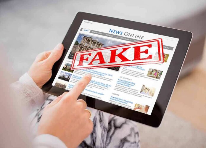 shutterstock_675861955.jpg Person holding a tablet displaying a news website with a 'FAKE' stamp