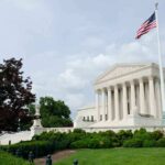 The U.S. Supreme Court building with an American flag and landscaped grounds