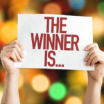 Hands holding a sign reading The Winner Is...