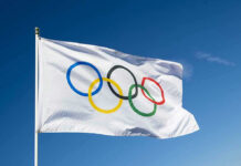 Olympic flag waving against clear blue sky.