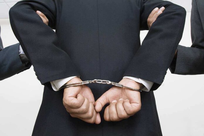 A person in a suit with hands cuffed behind their back