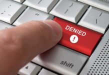 A finger pressing a red DENIED button on a computer keyboard