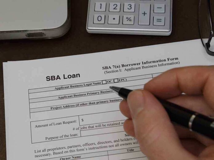 Hand filling out an SBA loan application form on a desk