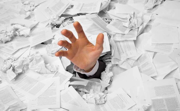 A hand reaching out from a pile of crumpled papers, symbolizing being overwhelmed by paperwork