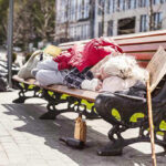 Person sleeping on park bench with cardboard sign.