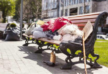 Person sleeping on park bench with cardboard sign.