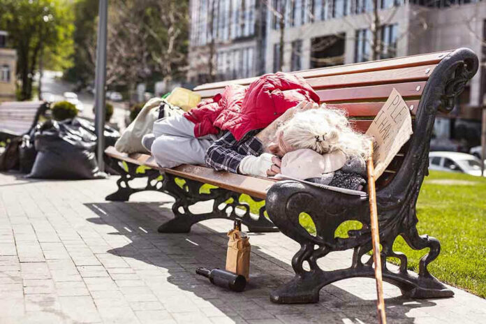 1100953052 Person sleeping on park bench with cardboard sign.