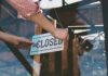 Hand placing closed sign on glass door