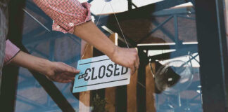 Hand placing closed sign on glass door