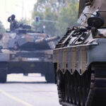 Tanks on a road with soldiers inside.