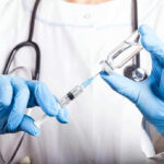 Doctor filling syringe with vaccine from vial.