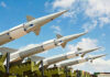Multiple missiles pointed upward on launchers against blue sky.