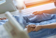 California EXPOSED: Billions STOLEN From Dying Americans Hospital patient holding visitors hand reassuringly.