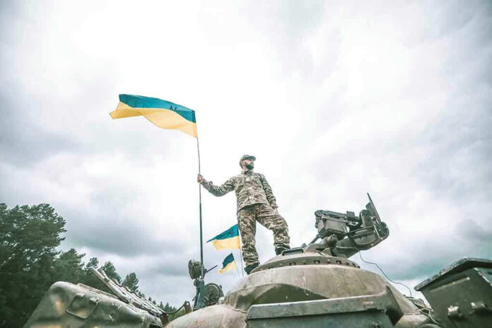 Soldier on tank holding Ukrainian flag.