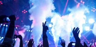 Crowd at a concert with hands raised and smoke effects in the background
