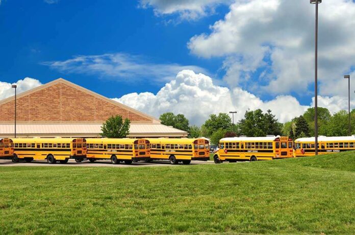 A row of yellow school buses parked in front of a school building under a cloudy sky