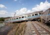 An overturned train on a railway track surrounded by vegetation