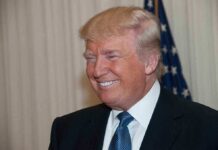 A smiling man in formal attire with an American flag in the background