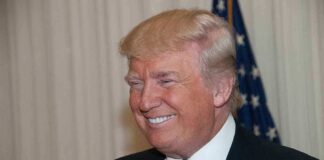 A smiling man in formal attire with an American flag in the background
