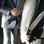 Two men shaking hands, one holding hidden knife.