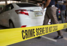 Crime scene tape blocking off white sedan.