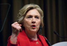 Person speaking passionately at a podium, wearing red jacket.