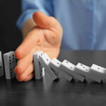 Hand stopping falling row of dominoes.